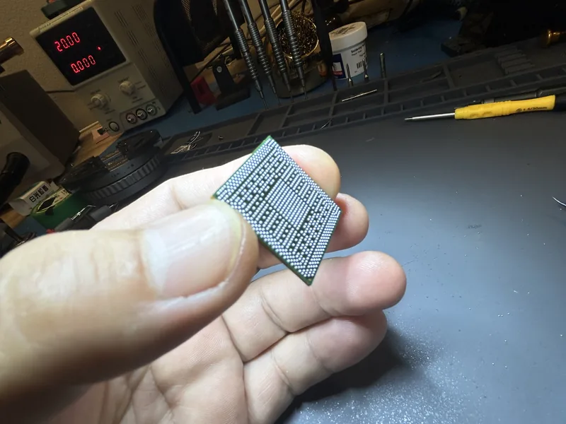 Chip removed from a board, held over the workbench with the power supply behind